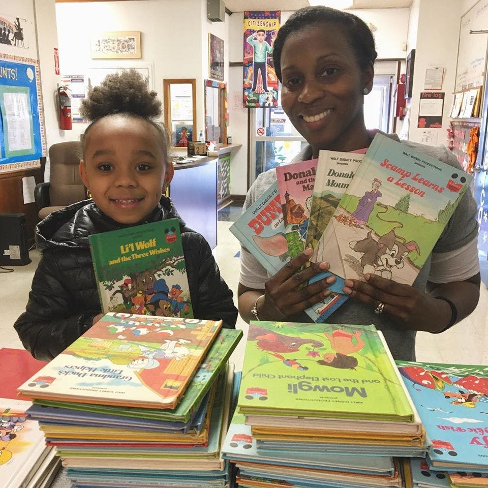 Person and child holding books, with stacks of books on a table