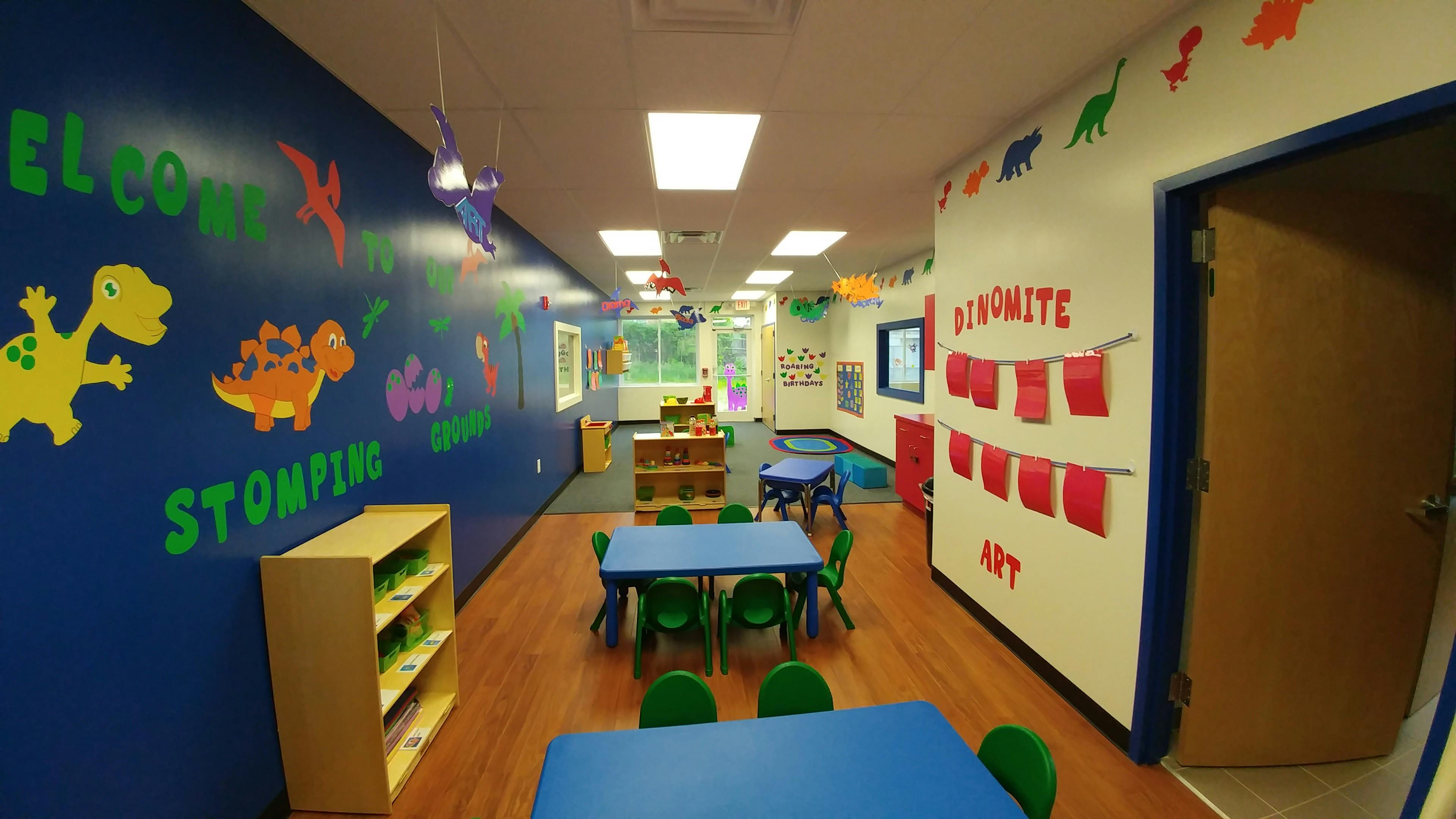 Classroom with blue walls and tables, dinosaur cutouts, and "DINOMITE ART" sign