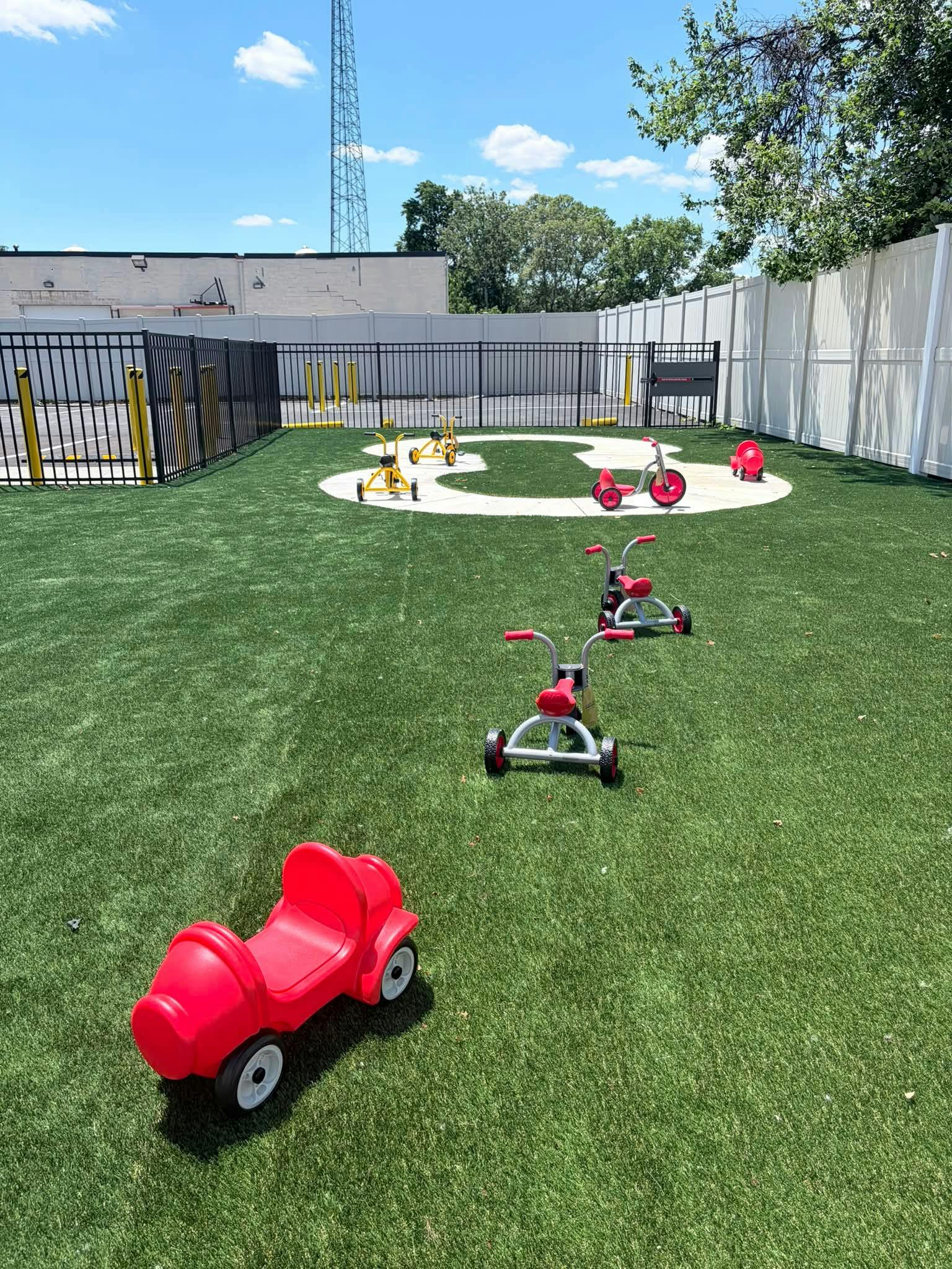 Plastic toy vehicles on a fenced playground with artificial grass