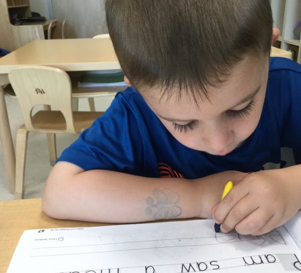 Child writing on paper with a yellow crayon