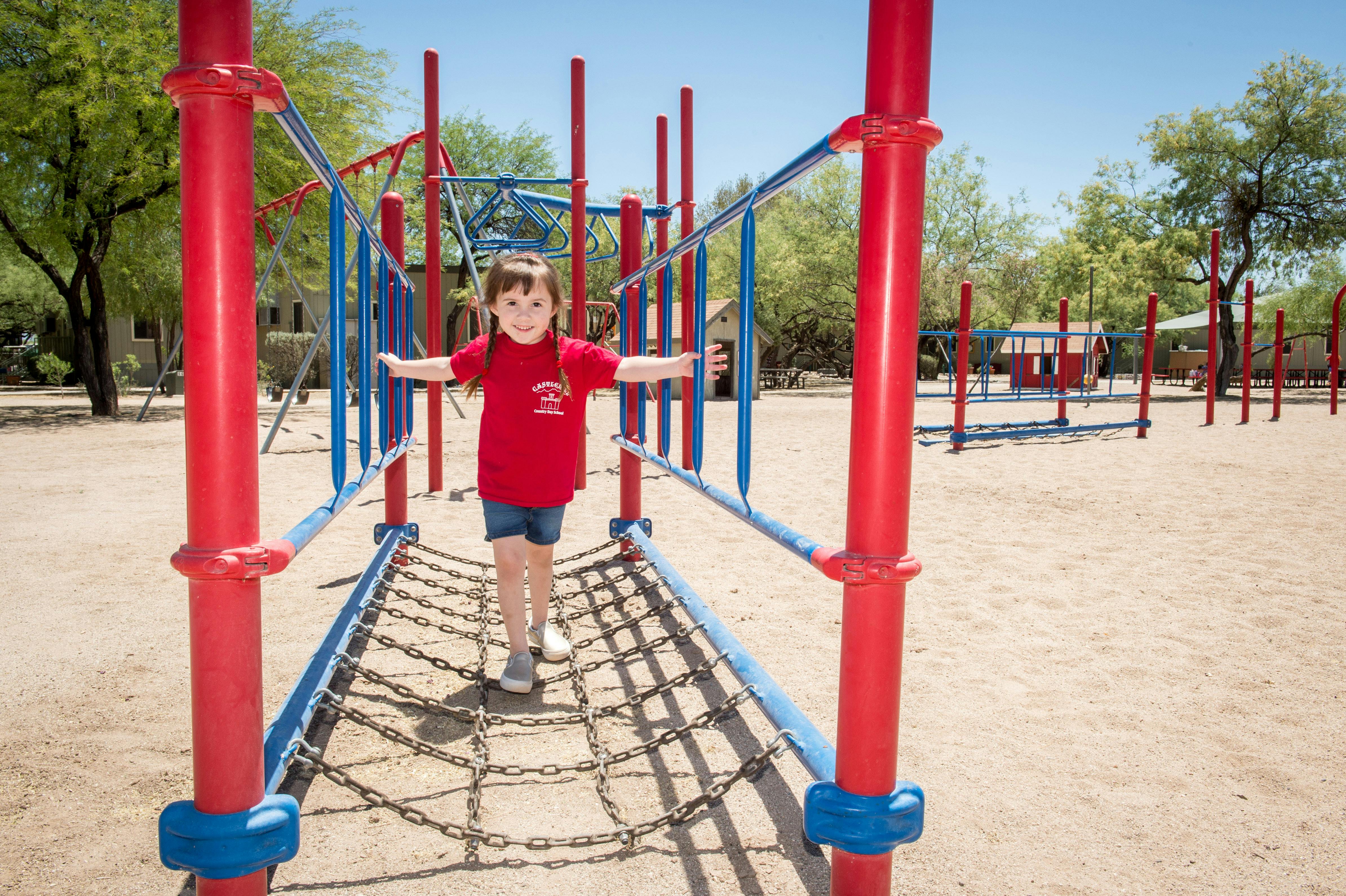 Child with arms out walking on a chain bridge at a playground