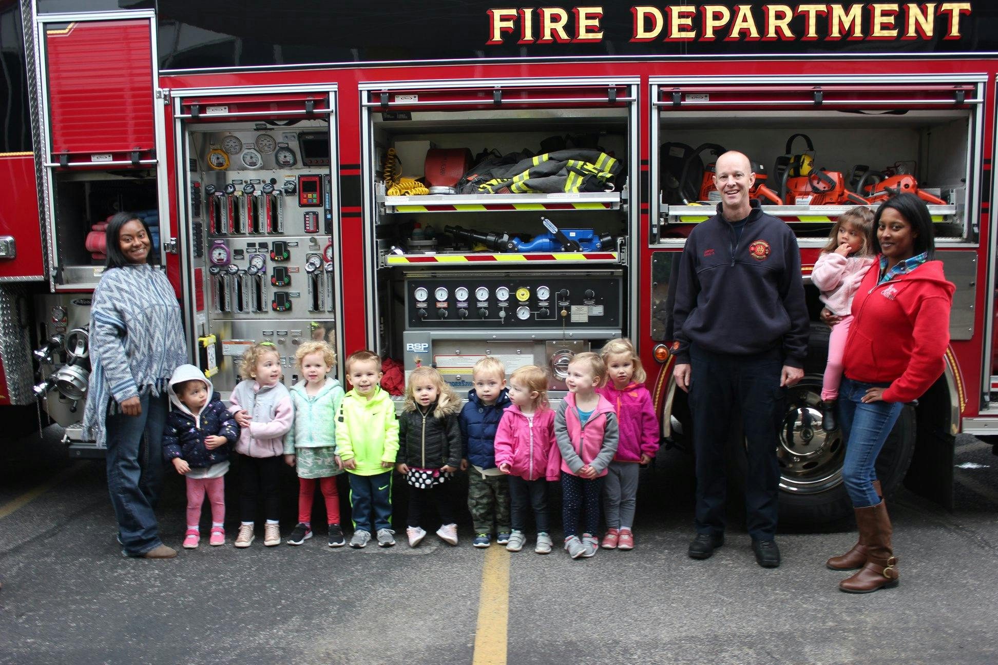 Adults and children standing in front of a fire truck with "FIRE DEPARTMENT" text