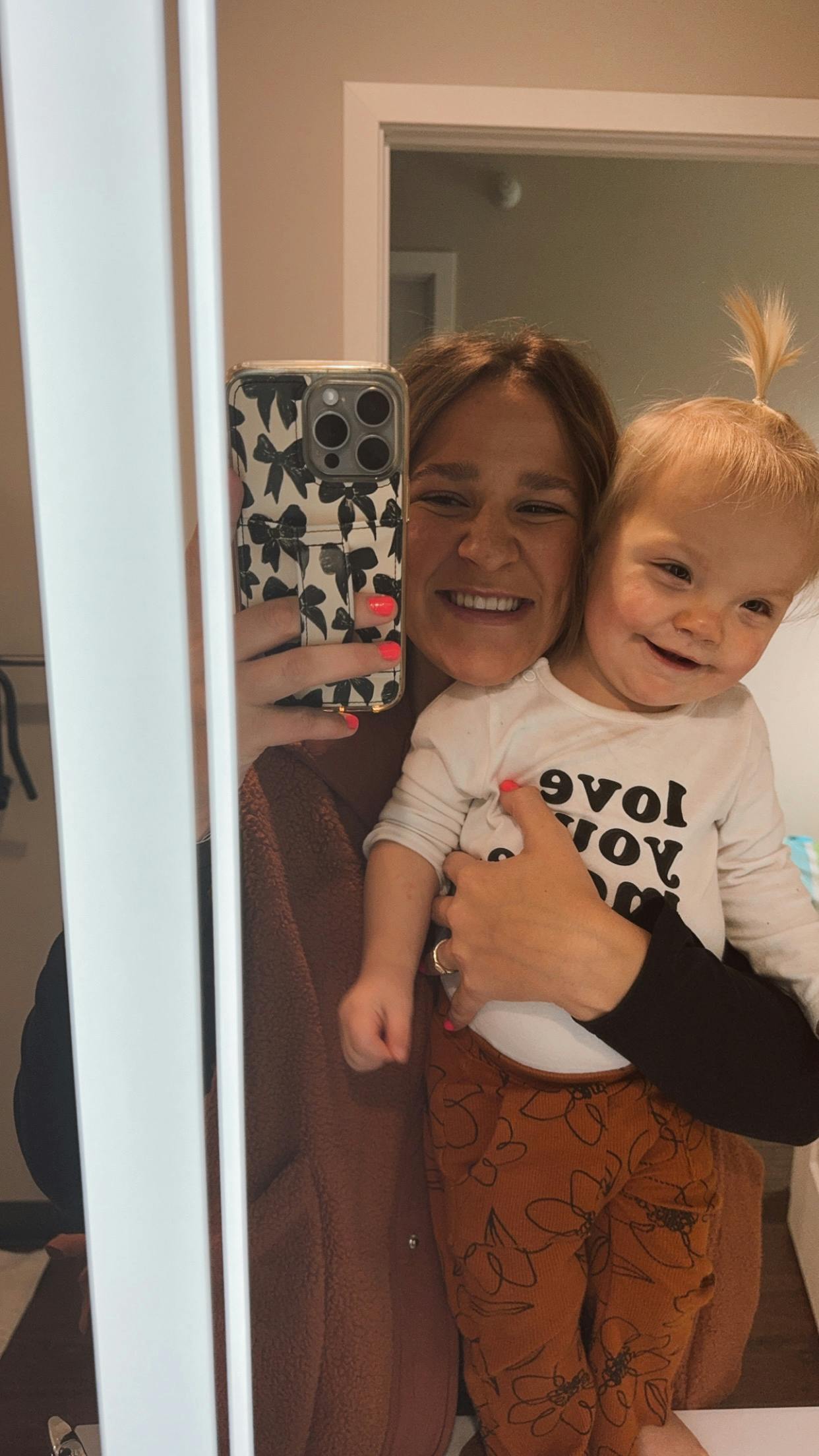 Person holding a child, both smiling at their reflection in a mirror