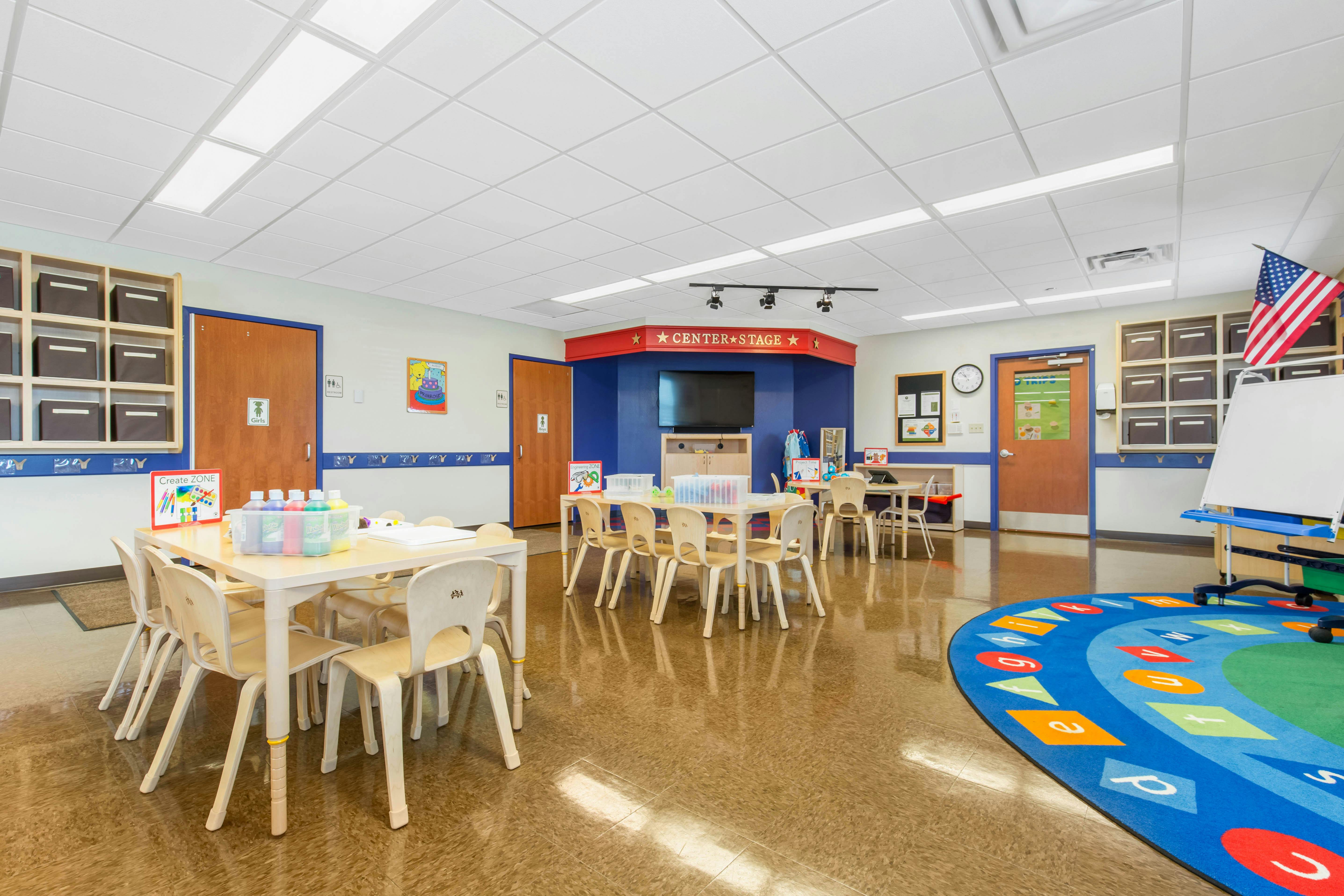 Classroom with small tables and chairs, a blue rug with letters and shapes