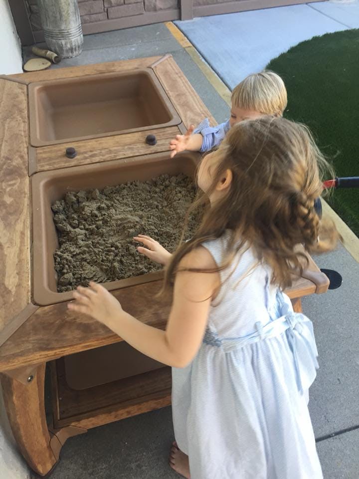 Two children playing with sand in a wooden sand table