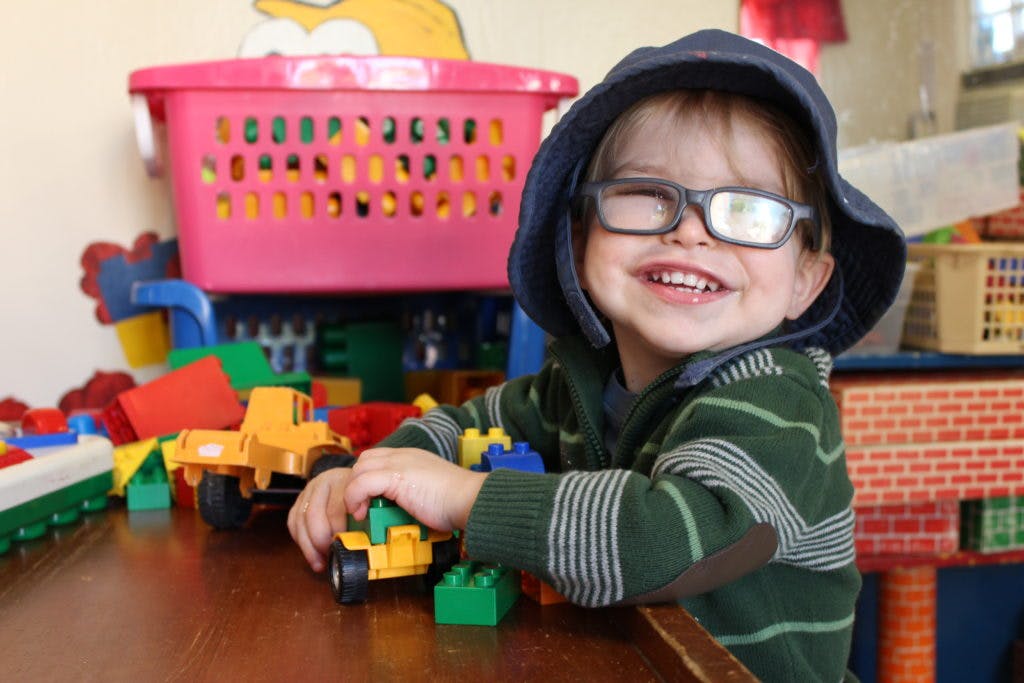 Child in glasses and hooded shirt playing with toy trucks and blocks