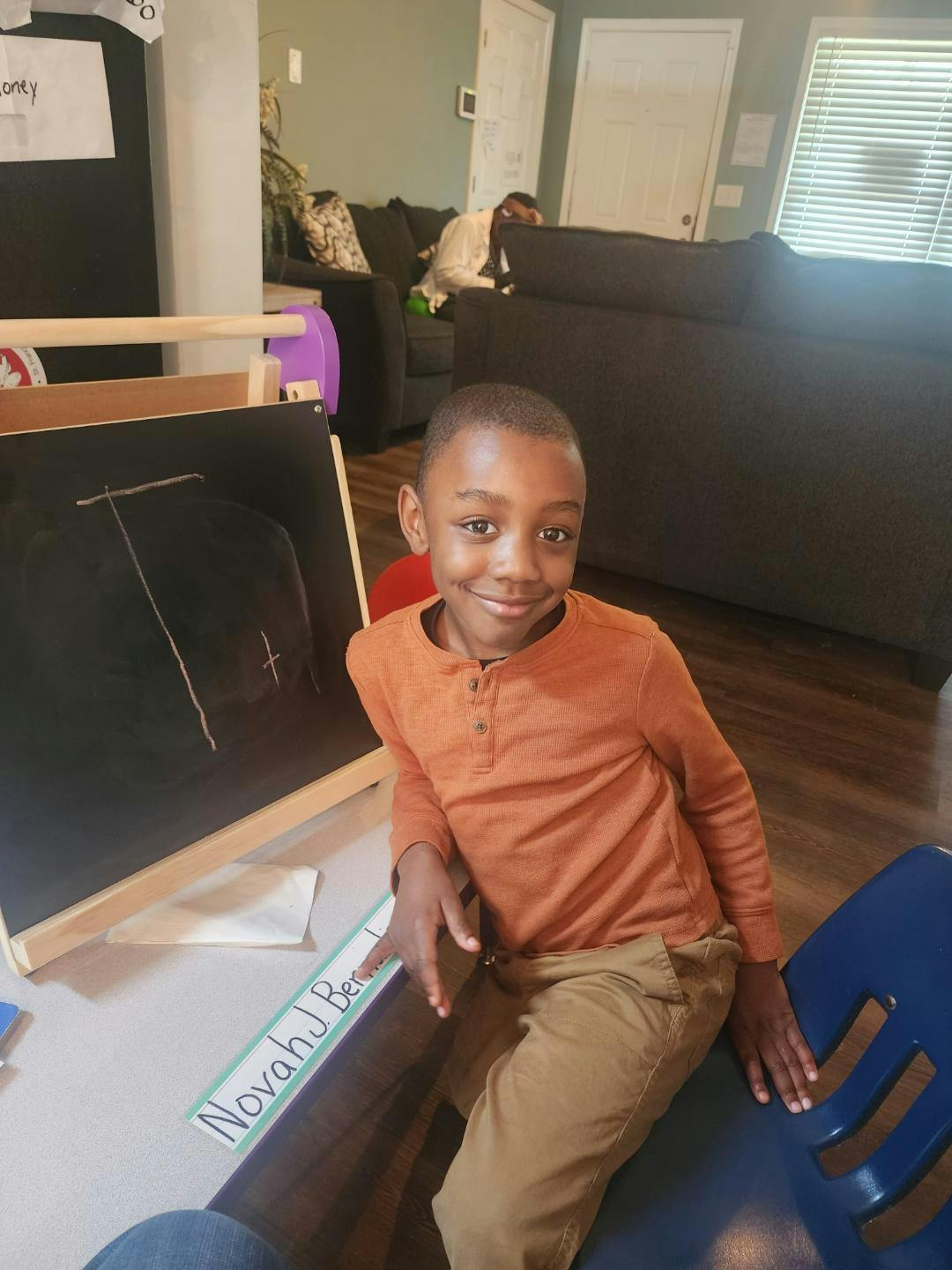 Child sitting next to a chalkboard with writing on it