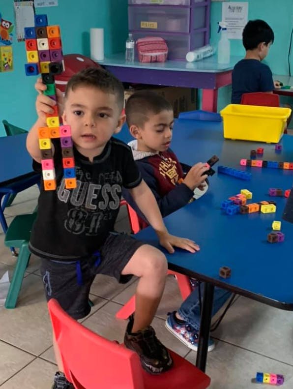 Child holding up a colorful block creation in a classroom