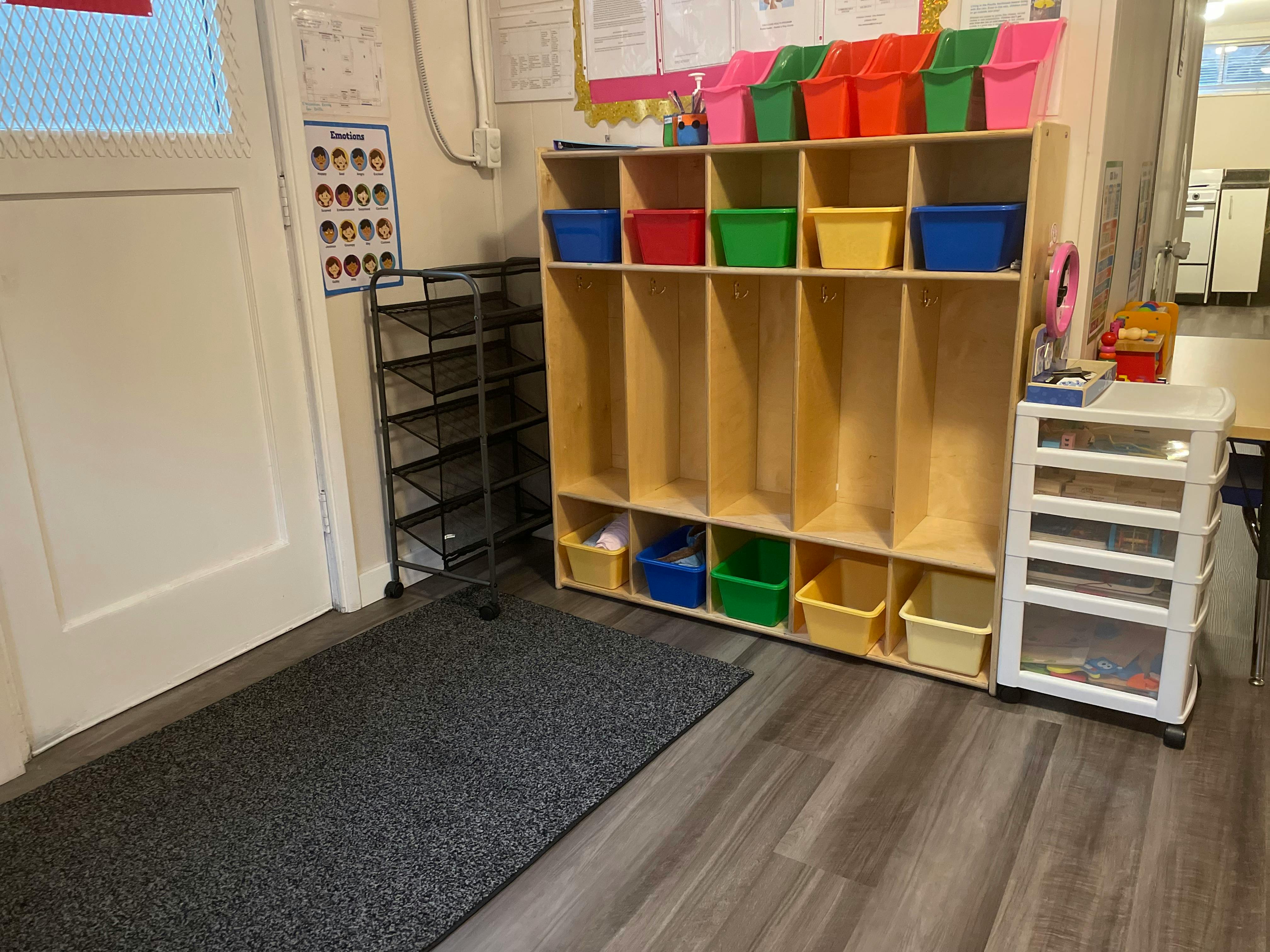 Classroom cubbies with colorful bins next to a door and shoe rack