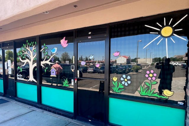 Storefront windows with cutouts of trees, birds, flowers, and a sun