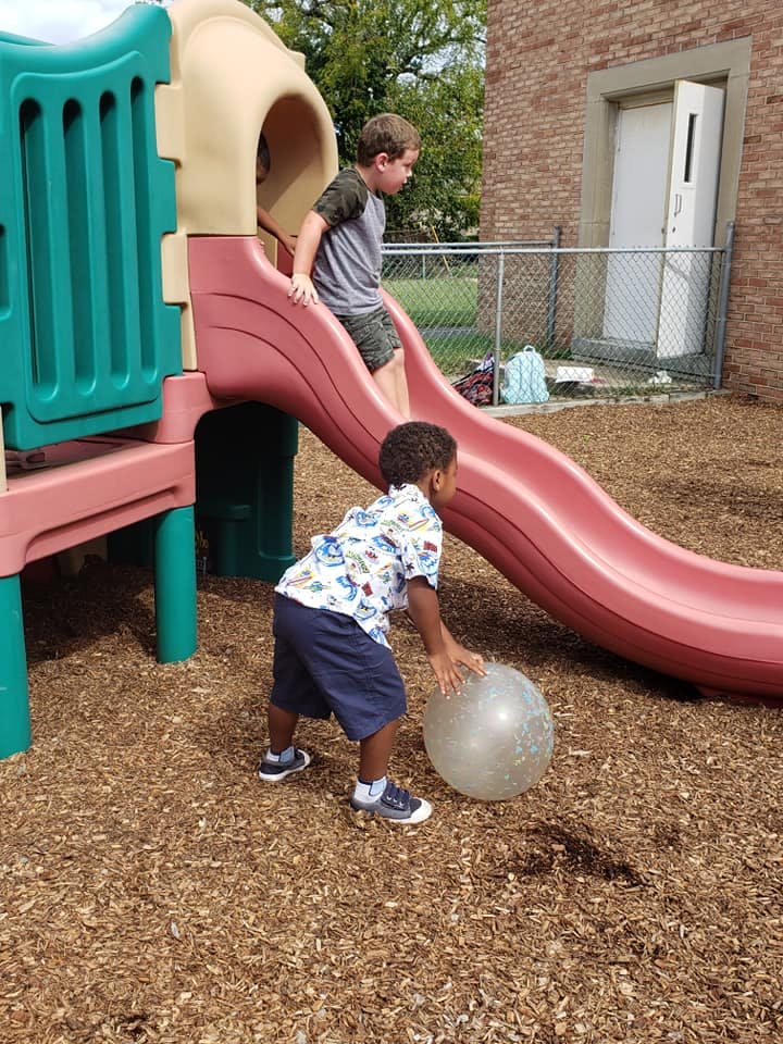 Two children playing on a playground slide with a ball