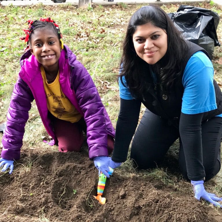 Child and person kneeling, digging in dirt with a small shovel