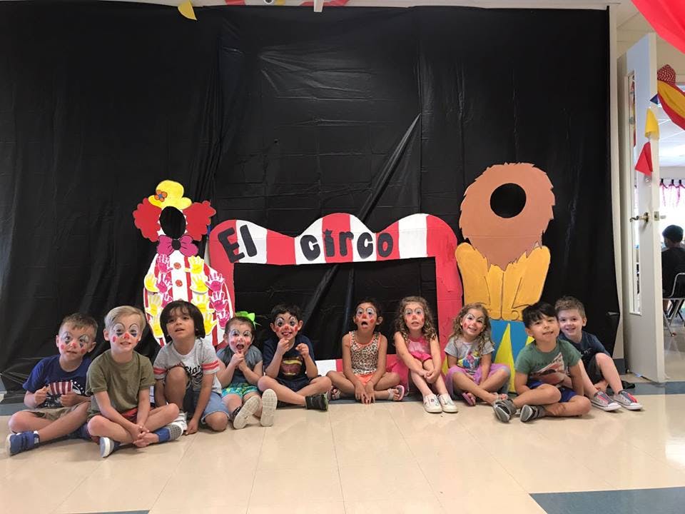 Group of children sitting in front of a circus-themed backdrop with "El Circo" sign