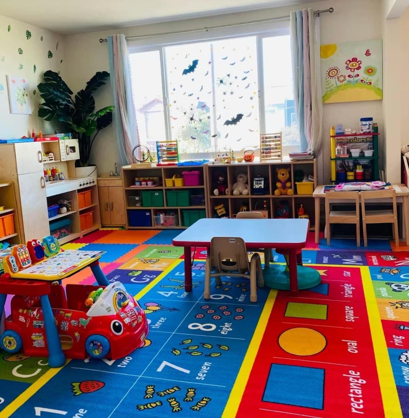 Playroom with colorful rug, small tables and chairs, and shelves with toys