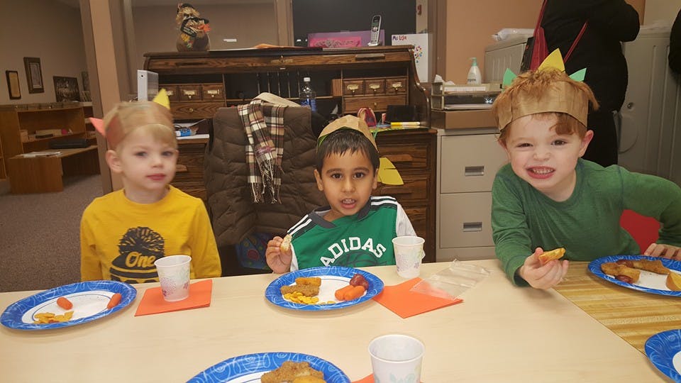 Three children wearing paper crowns sitting at a table with plates of food