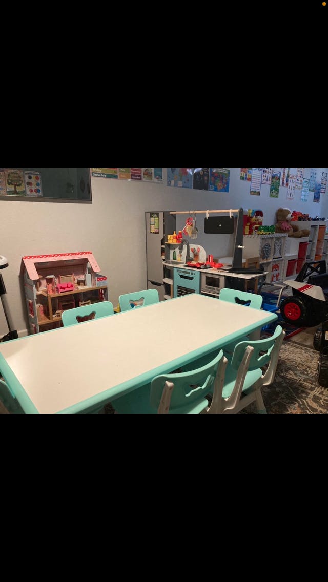 Long white table with teal chairs in a playroom with toys and dollhouse