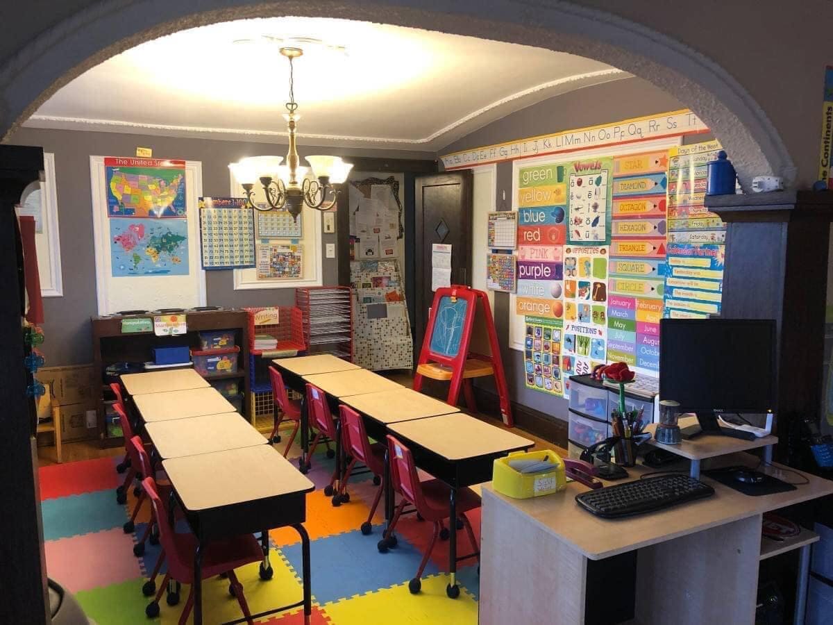 Classroom with rows of desks and chairs, colorful wall charts, and a computer