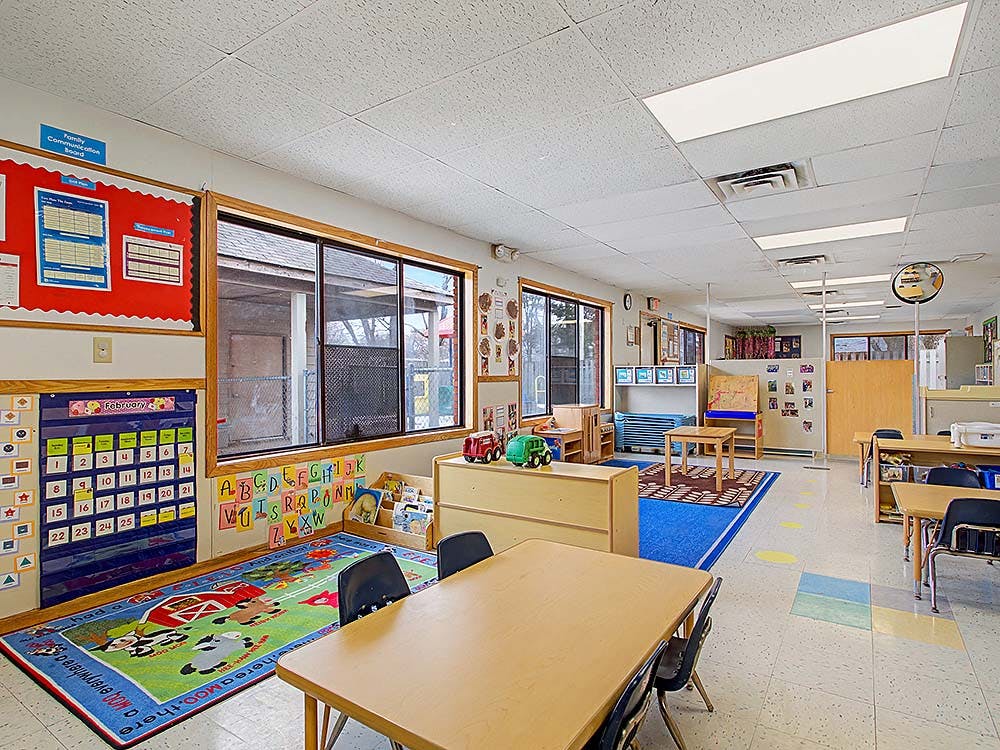 Empty classroom with small tables, chairs, and colorful rugs on the floor