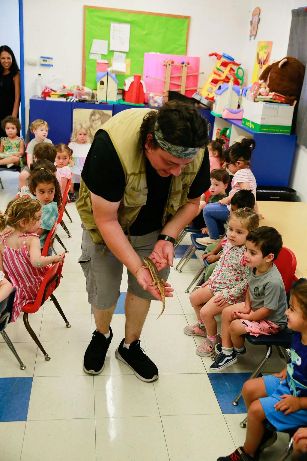 Person holding a lizard for children sitting in chairs in a classroom
