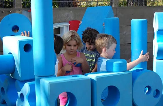Three children playing with large blue building blocks