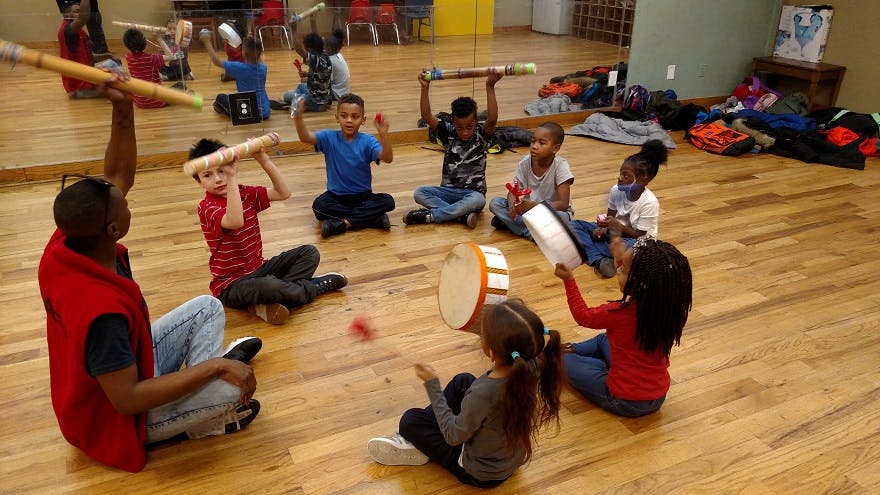 Person and children sitting in a circle playing drums and holding instruments