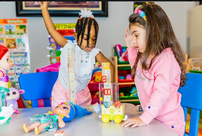Two children playing with building blocks and dolls at a table