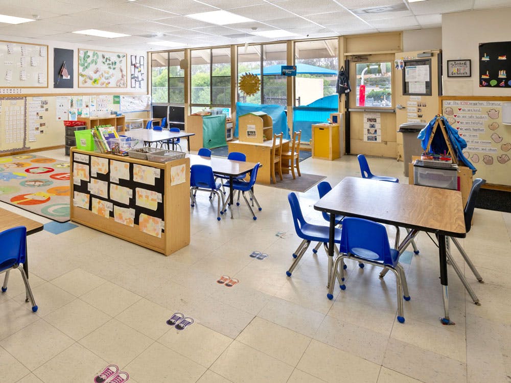Empty classroom with small tables, blue chairs, and children's artwork on walls