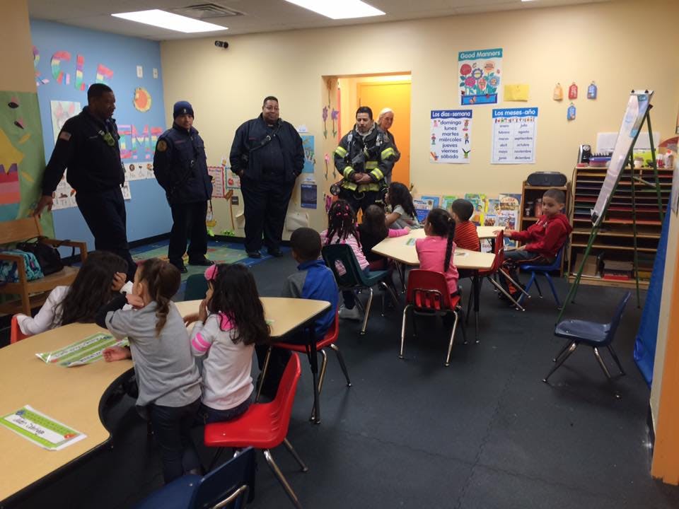 Adults in uniform standing in a classroom with children seated at tables