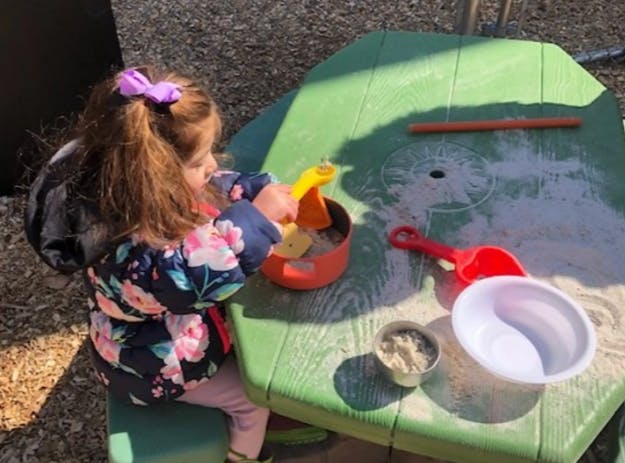 Child playing with sand and toys at a green table
