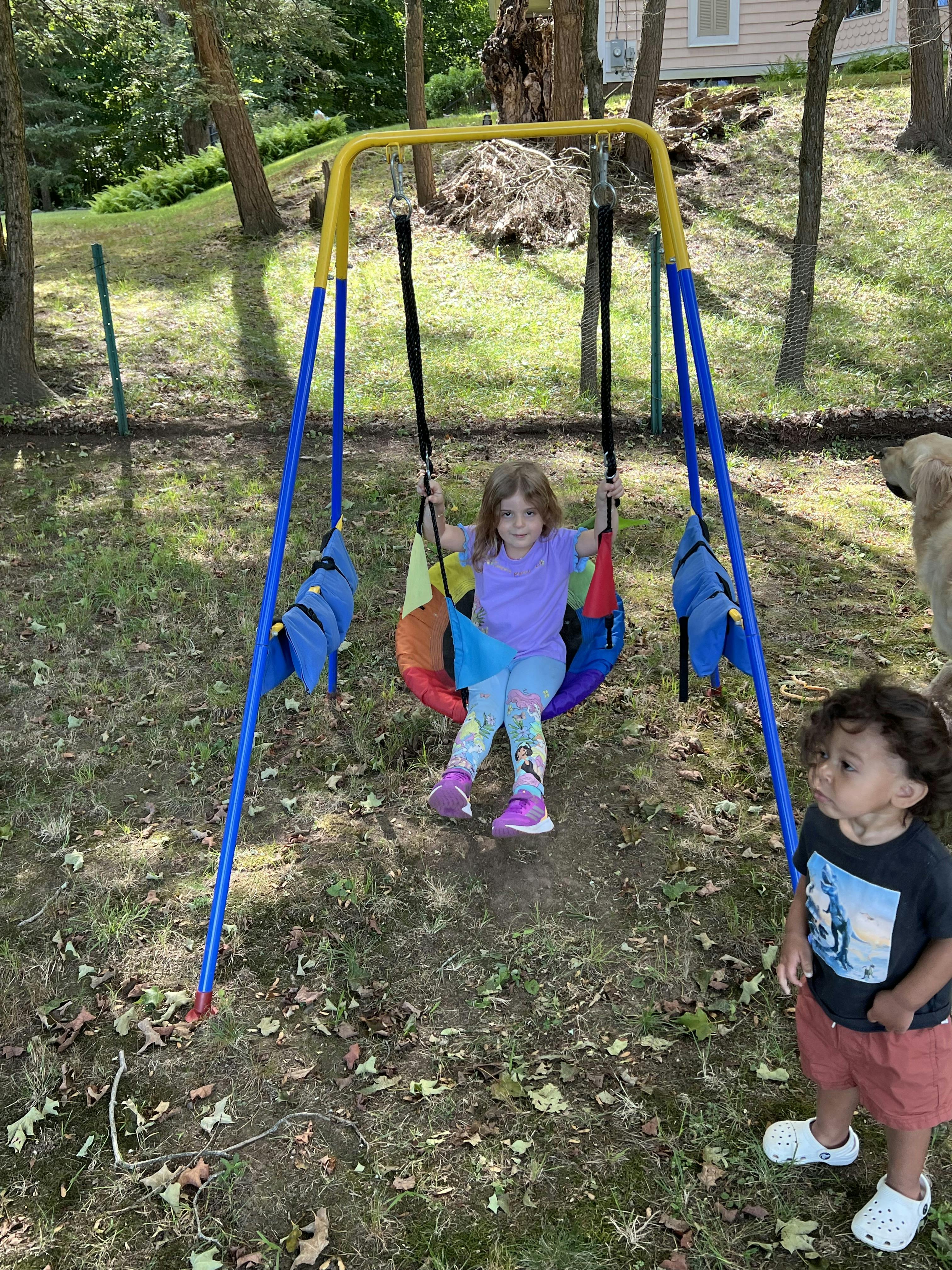 Child sitting in a swing set with another child standing nearby