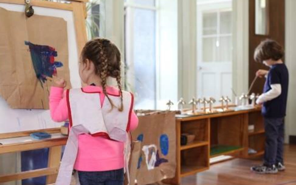 Child painting at an easel, another child playing with objects