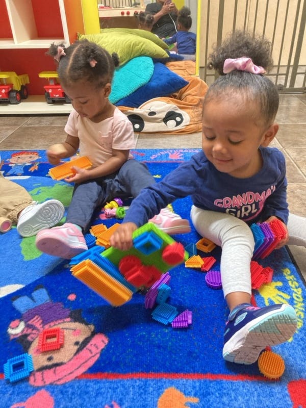 Two children sitting on a rug playing with colorful building blocks