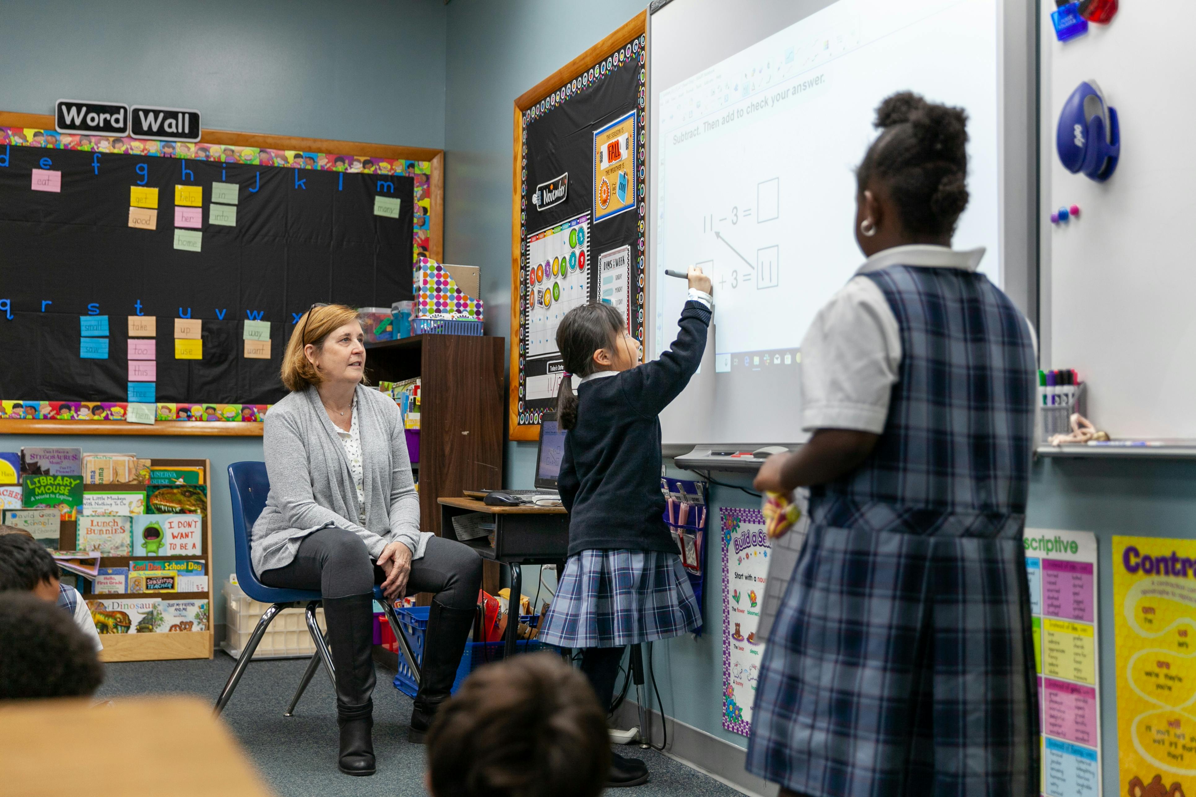 Adult and two children in a classroom, one child writing on a whiteboard