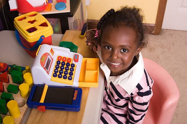 Child smiling while sitting at a table with a toy cash register