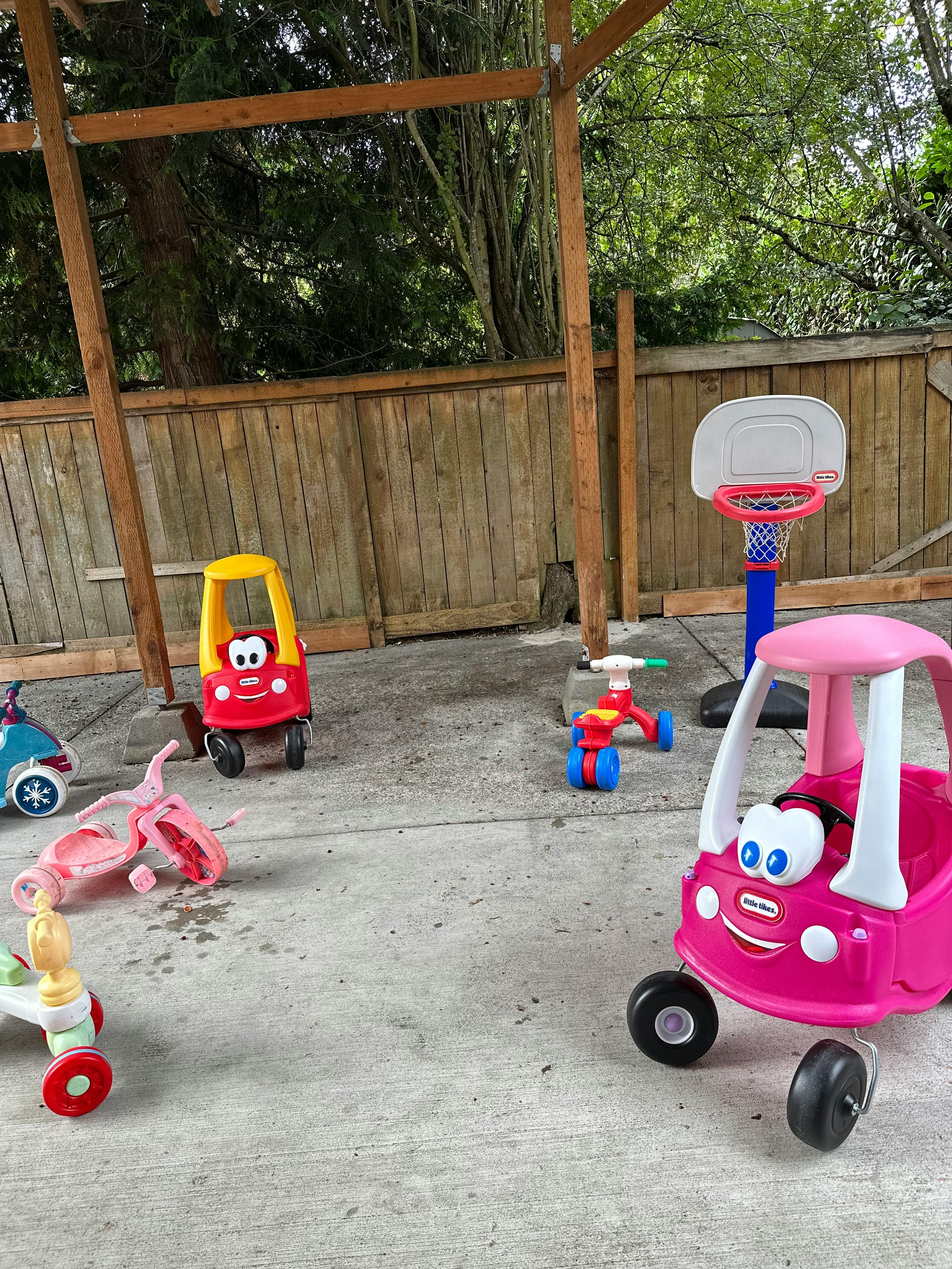 Children's ride-on toys and a small basketball hoop on a paved surface