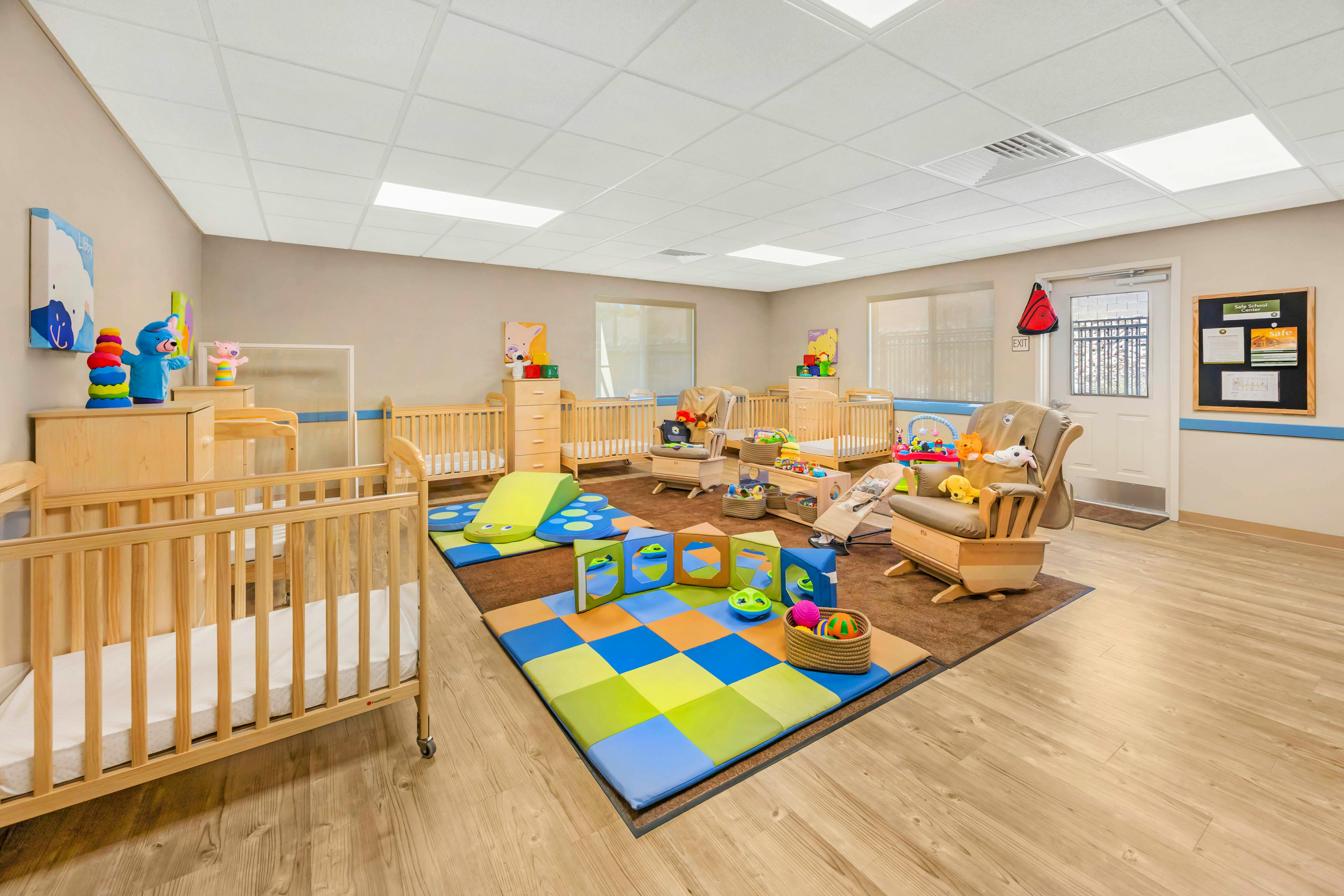 Daycare room with multiple cribs, rockers, and colorful play mats on the floor