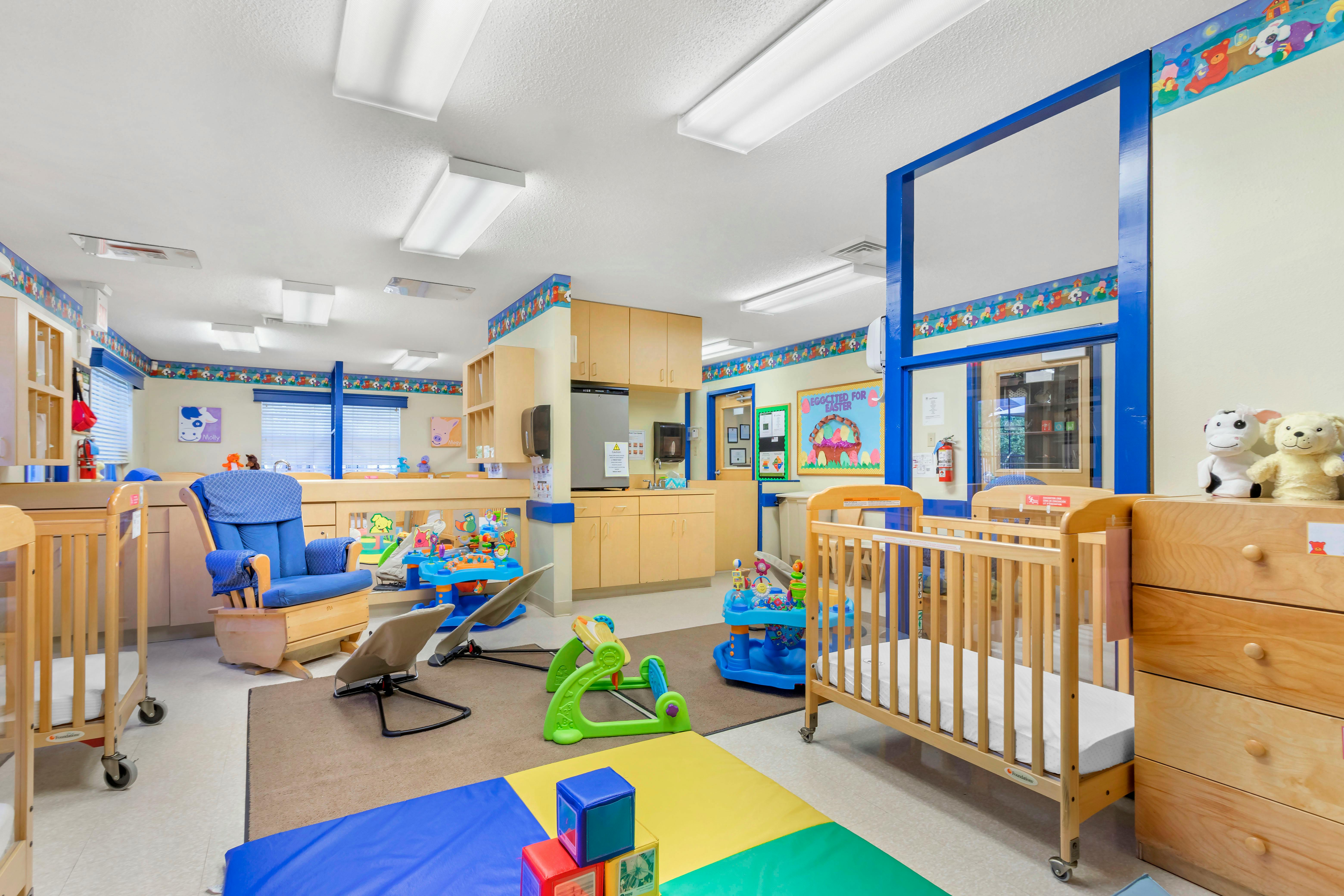 cribs, changing station, and play area in a daycare room