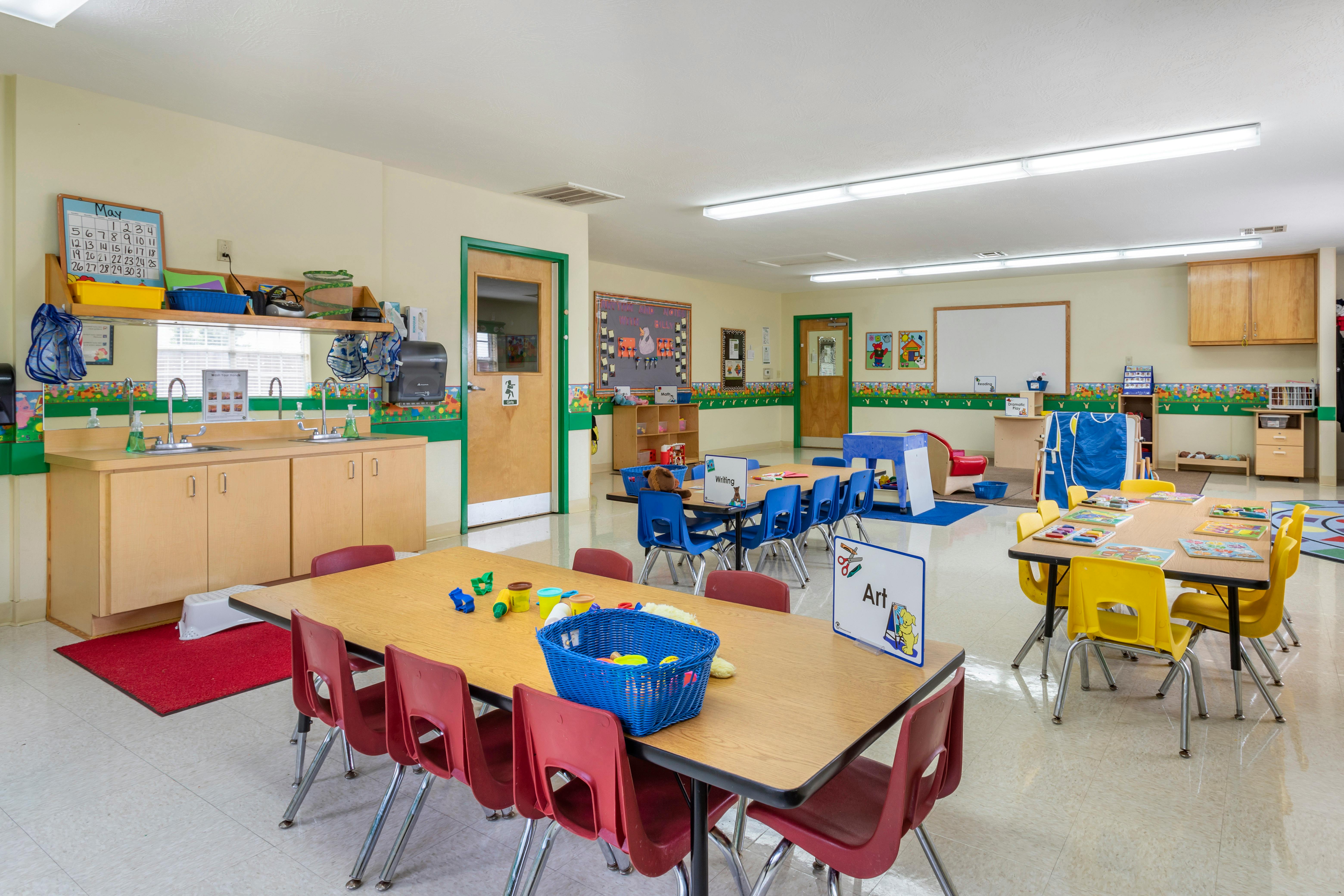 Classroom with multiple tables and chairs, a sink counter, and wall decorations