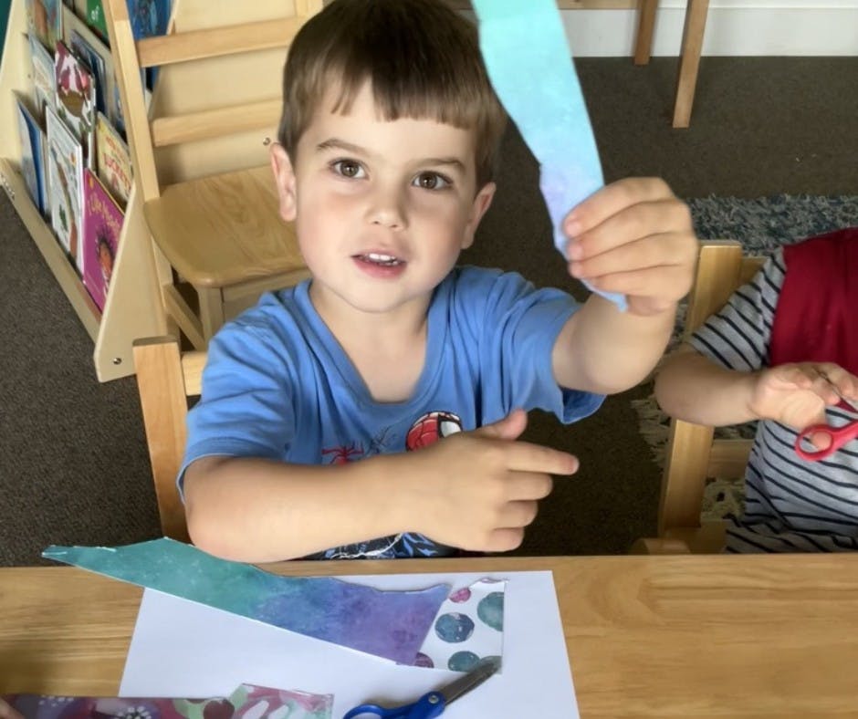 Child holding up a piece of paper while sitting at a table with crafts