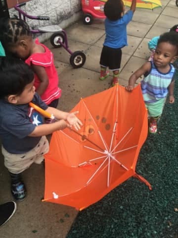 Children playing with an orange umbrella outdoors