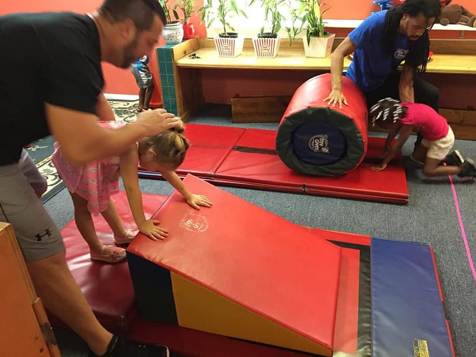Two adults assisting children on gymnastics equipment