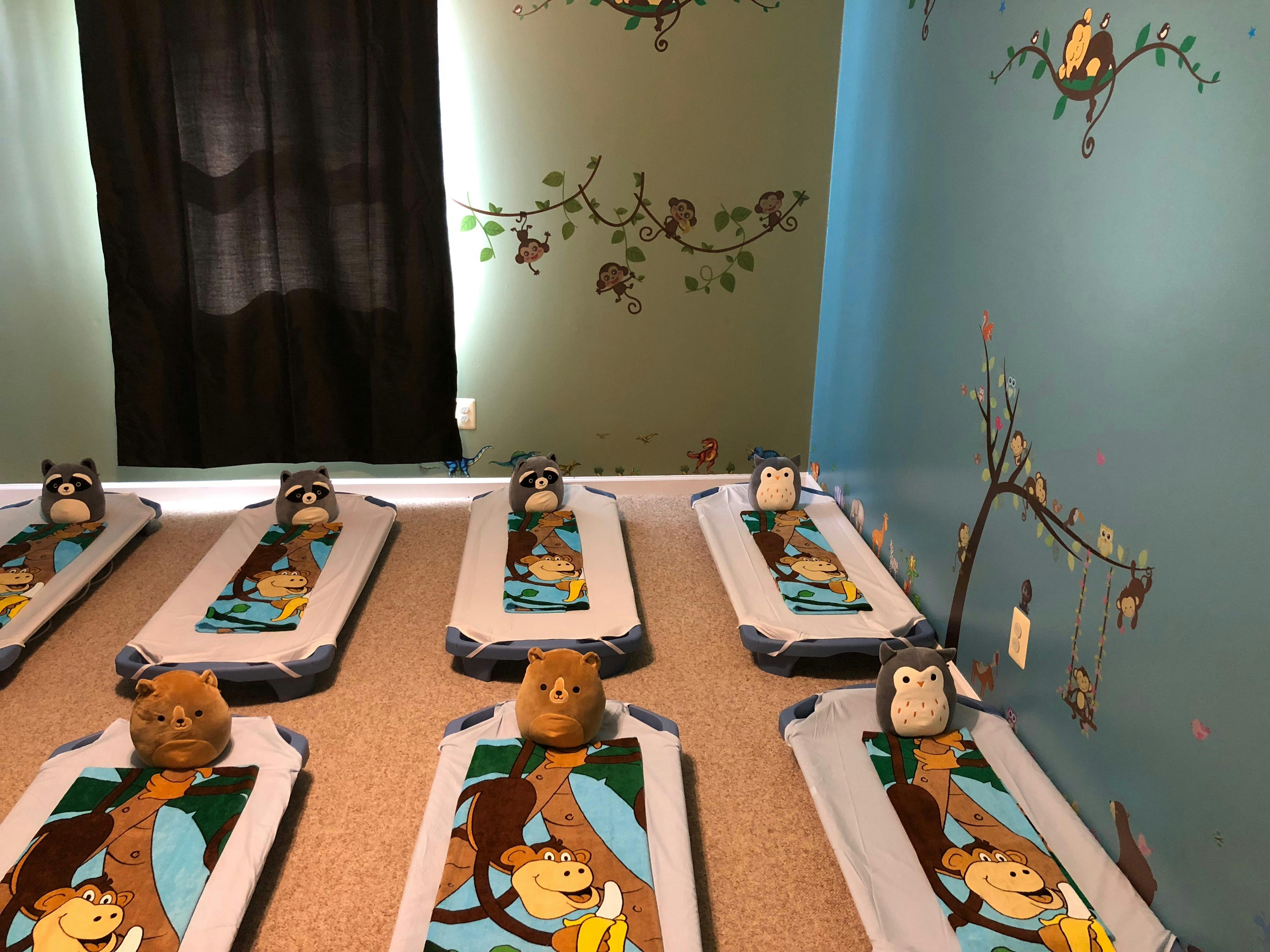Multiple cots with animal-themed blankets and stuffed animals