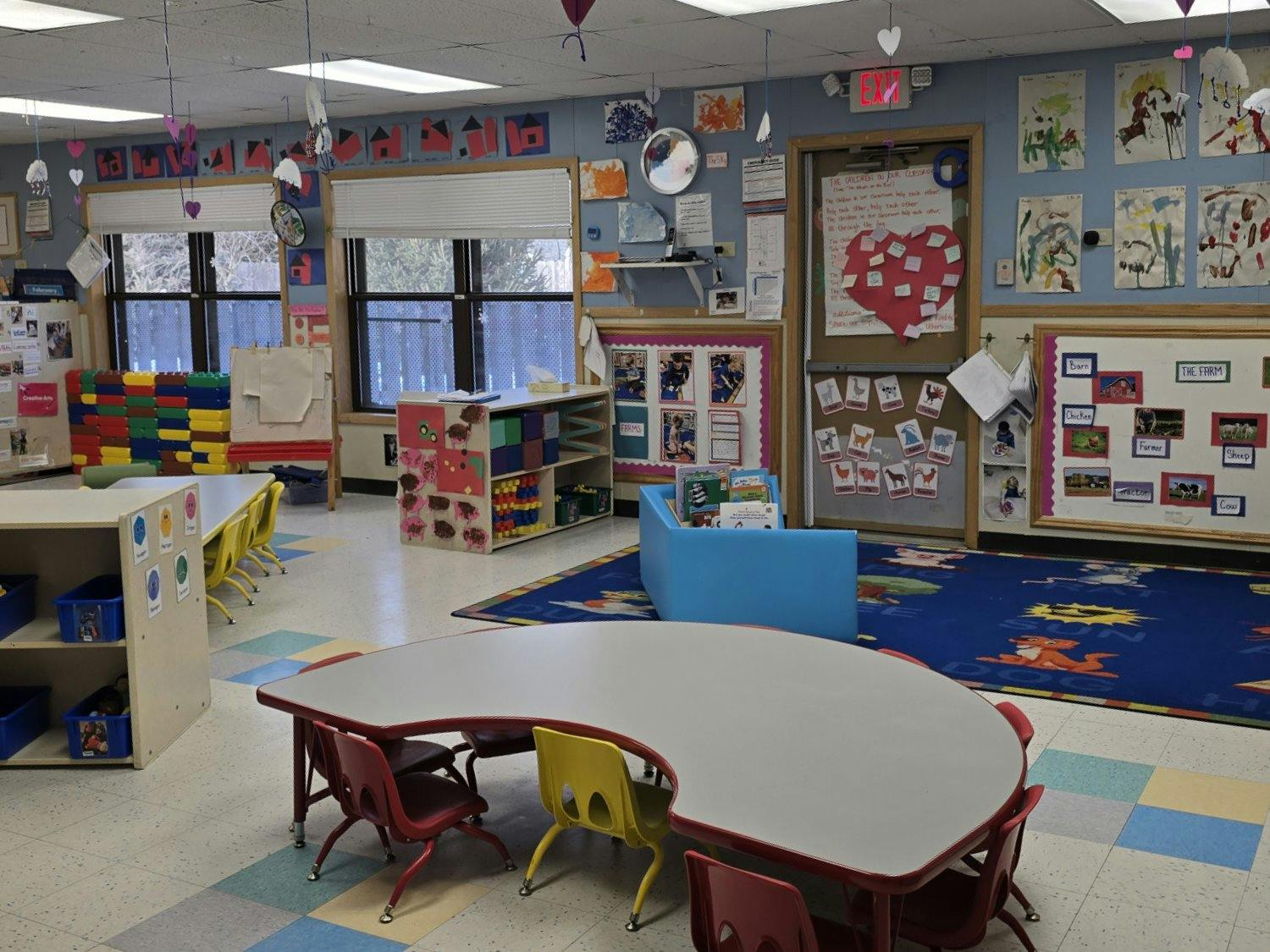 Classroom with small tables and chairs, colorful carpet, and windows with blinds