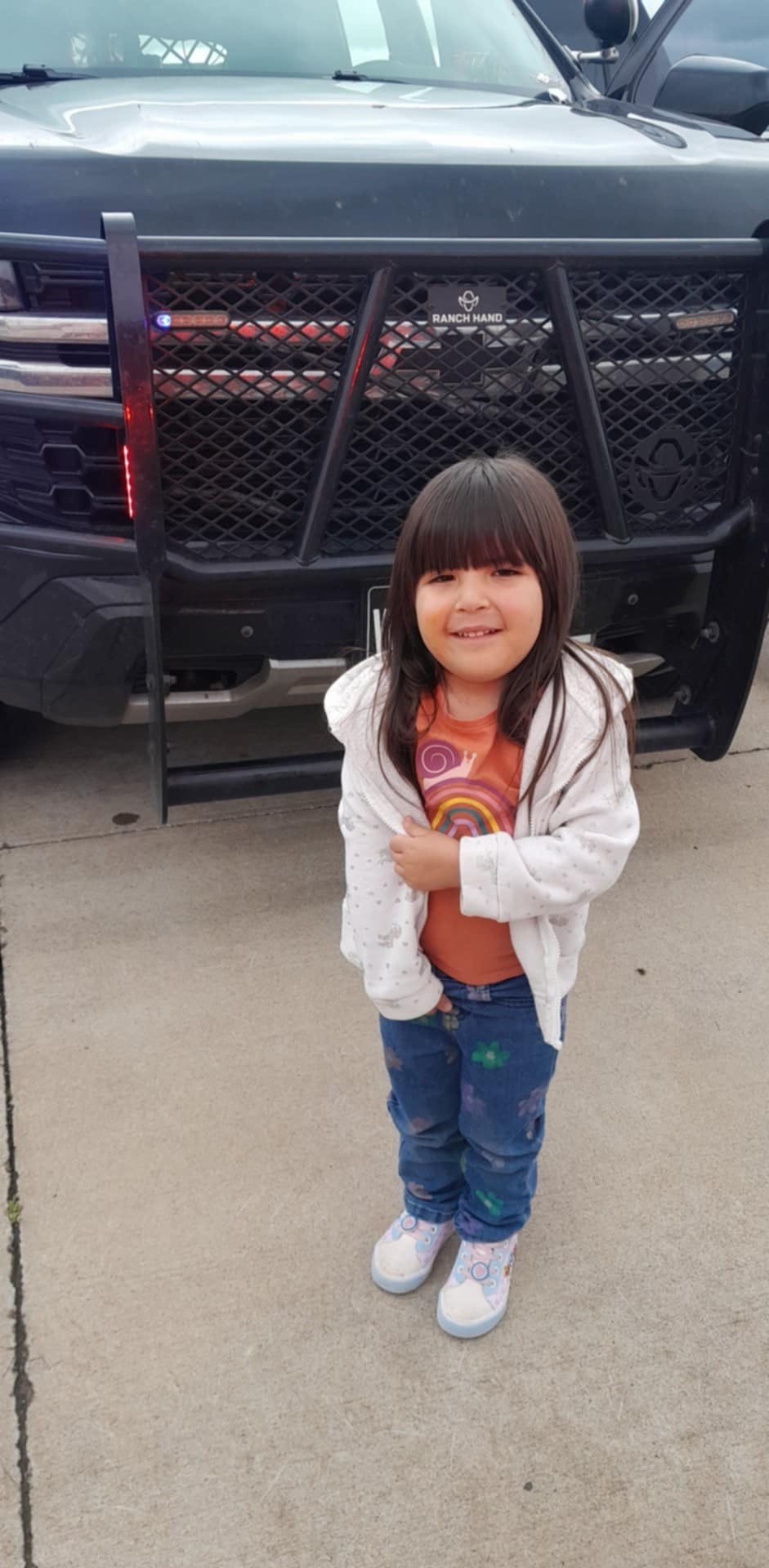 Child standing in front of a vehicle with a grill guard