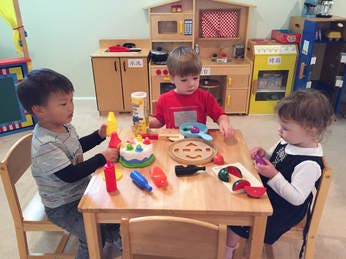 Three children playing with toy food at a small table