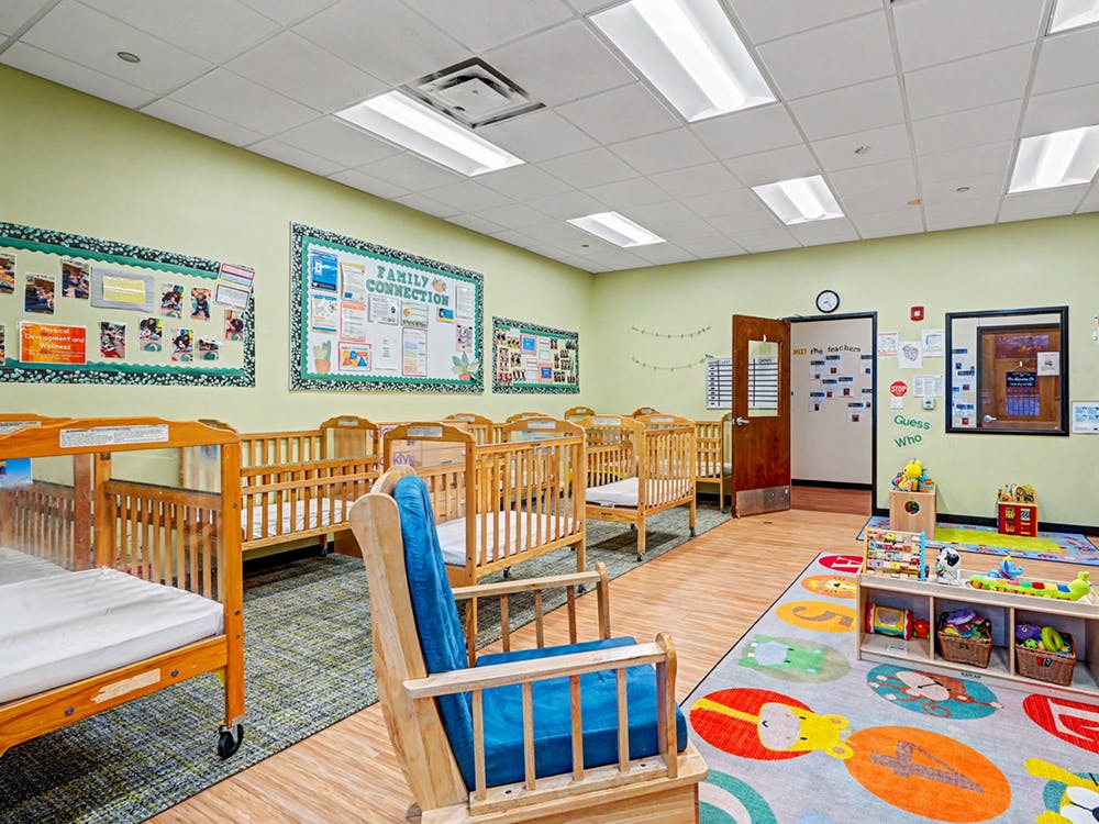 cribs in a bright daycare room with a rocking chair and colorful rug