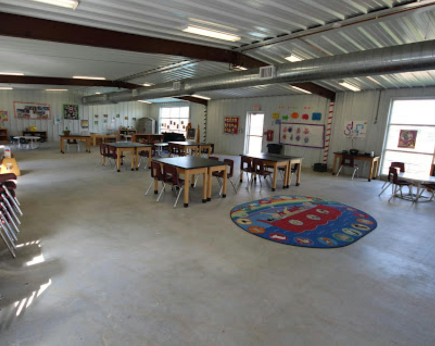 Classroom with small tables and chairs, and a colorful rug on the floor