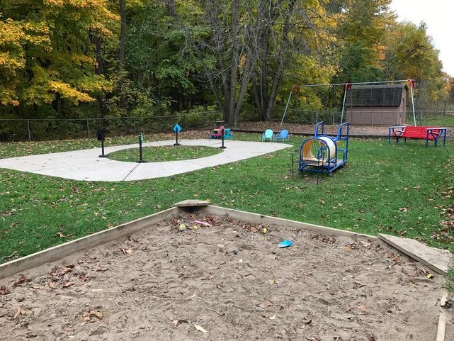 Outdoor playground with a sandbox, swings, and a small tunnel