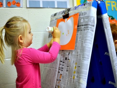 Child applying glue to a paper apple on an easel