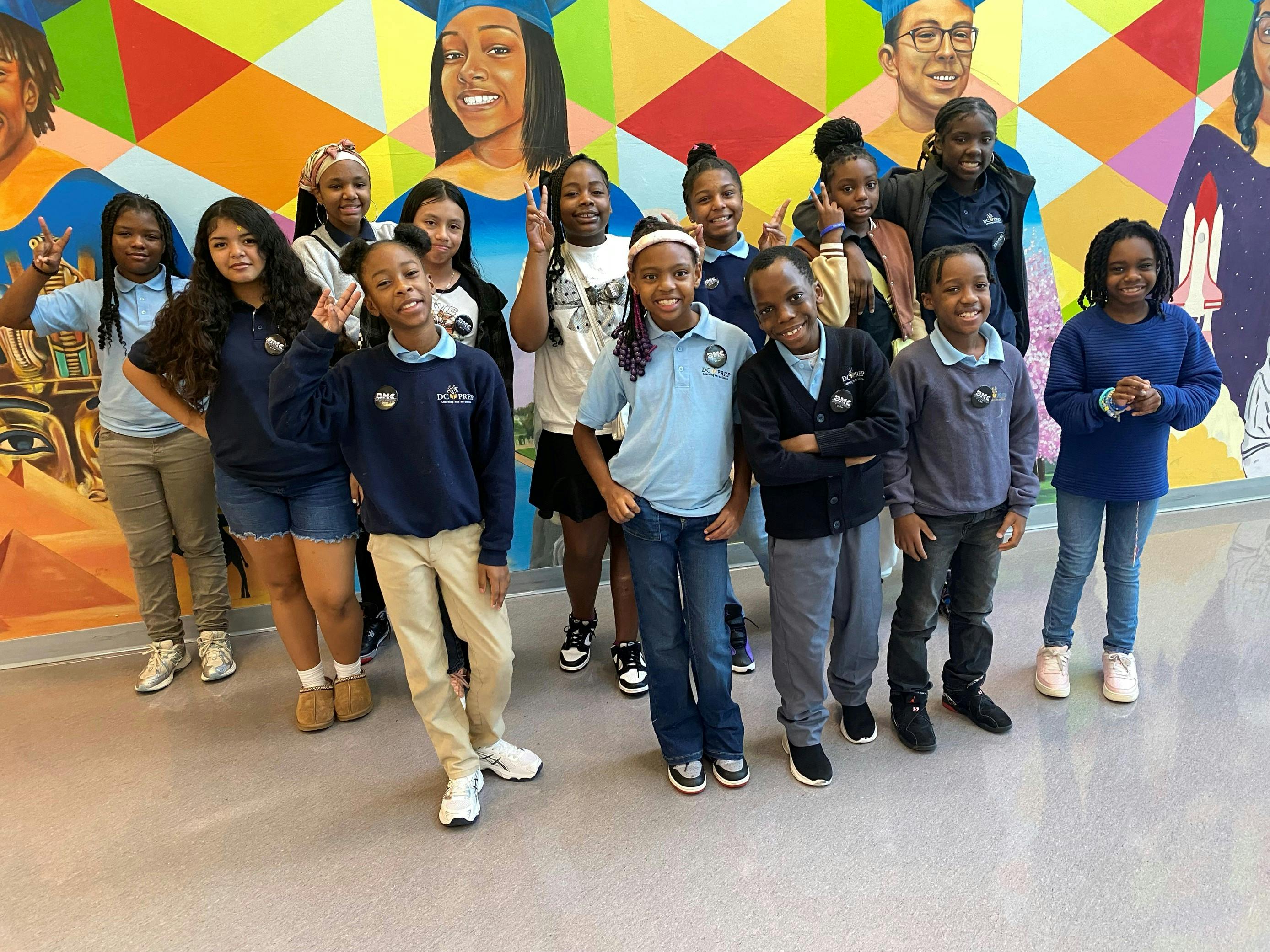 Group of children and teens standing in front of a colorful mural